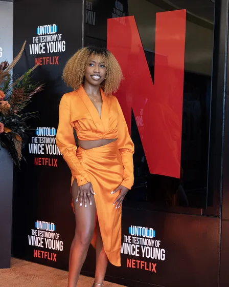 Guest in an orange dress in front of the backdrop